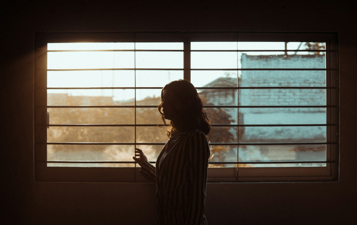 Mujer mirando hacia el exterior a través de una ventana.