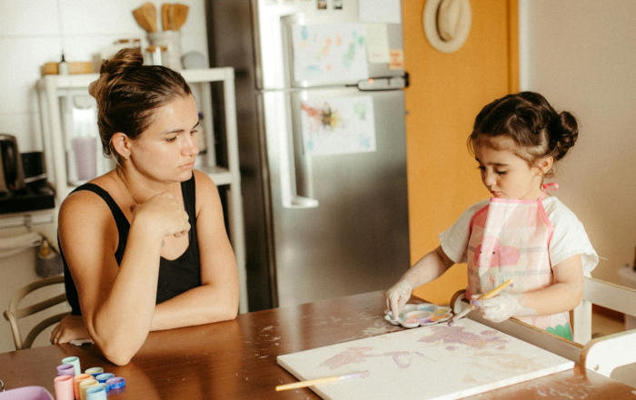 Una madre observa a su hija mientras pinta en la mesa familiar.