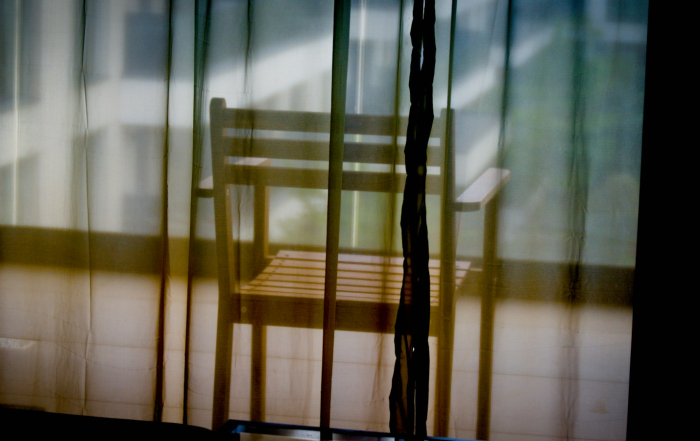 Silla de madera tras cortinas translúcidas en un espacio silencioso.