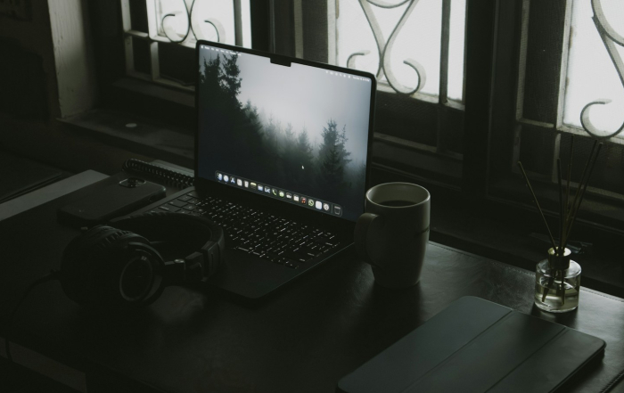 Escritorio real con computador, audífonos y taza junto a la ventana.