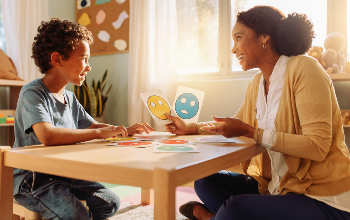 Niño afrocolombiano identifica emociones mediante tarjetas ilustradas con una psicóloga infantil. Imagen ilustrativa creada con IA.