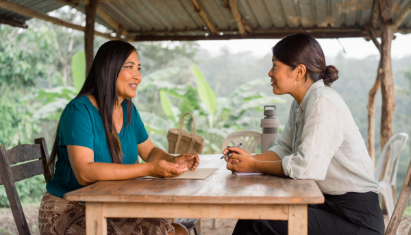 Mujer indígena dialoga con facilitadora comunitaria en una representación ilustrativa de orientación.